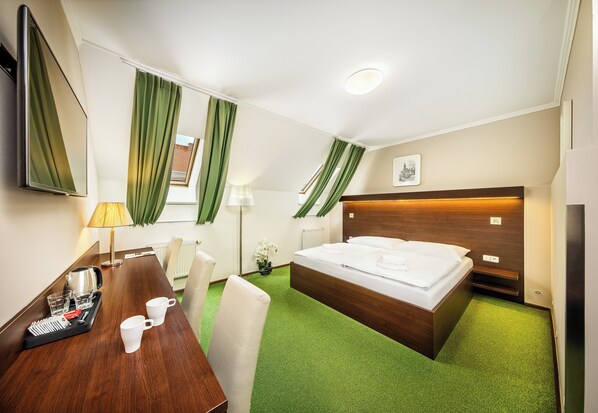 Une chambre d’hôtel avec un lit, un bureau avec une chaise, une lampe et une fenêtre avec des rideaux.