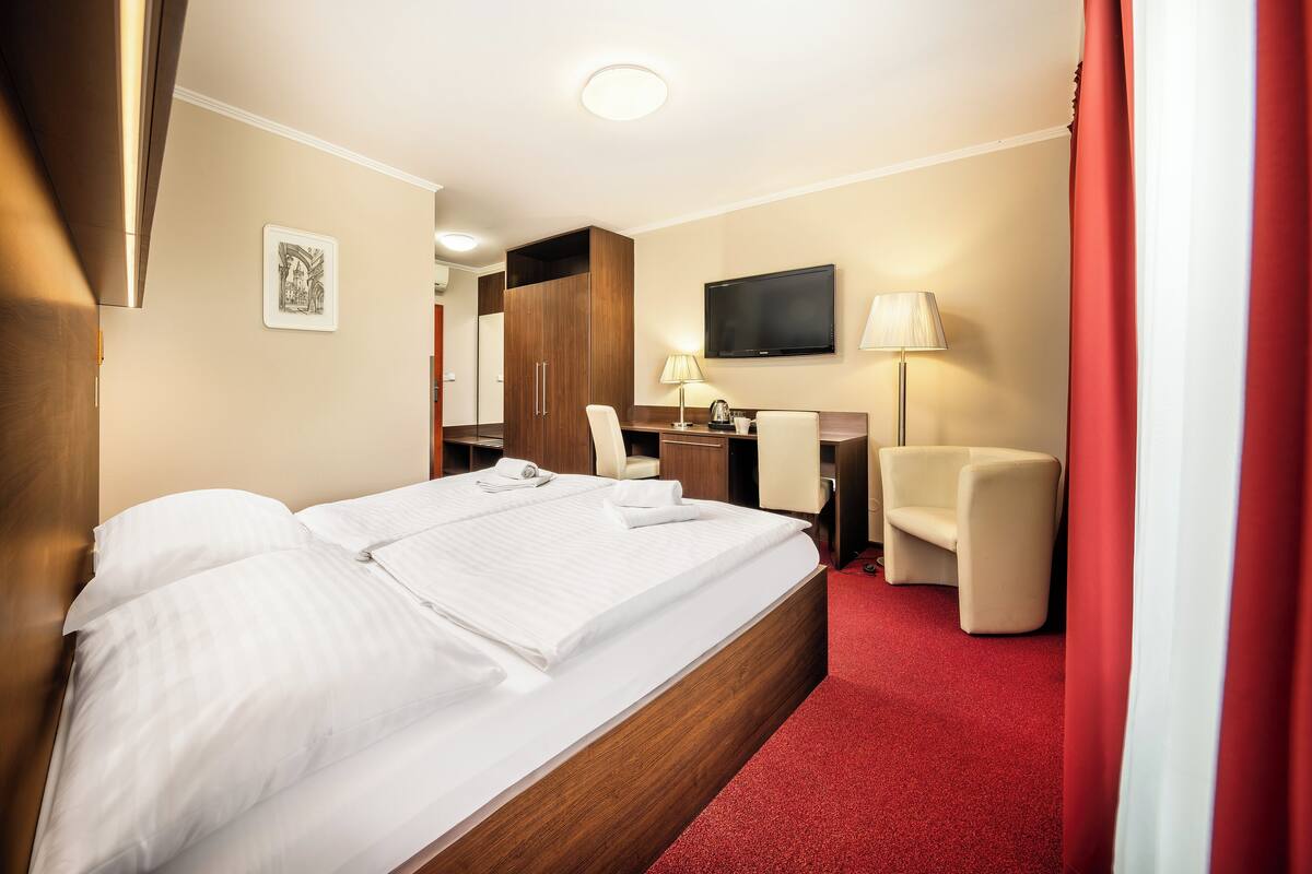 Une chambre d’hôtel avec un grand lit, un bureau, une chaise, une télévision et une moquette rouge.