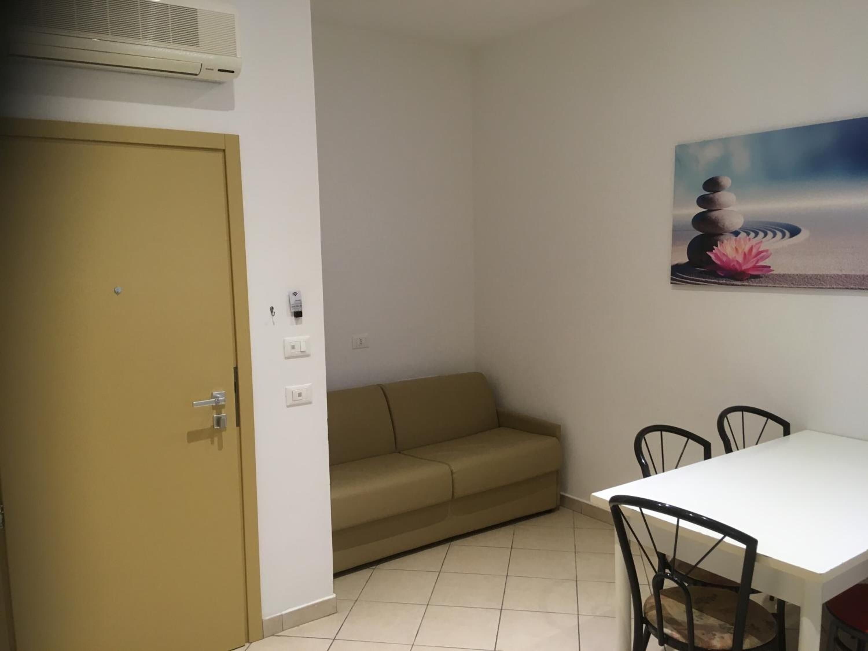 A room with a beige sofa, a white table with black chairs, a painting of stones and a lotus flower, and a door with a keyhole.
