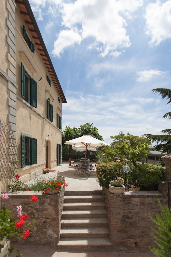 A courtyard with a staircase leading to a building with green shutters, outdoor seating, and potted plants. - Villa Cristina (Castellina in Chianti)