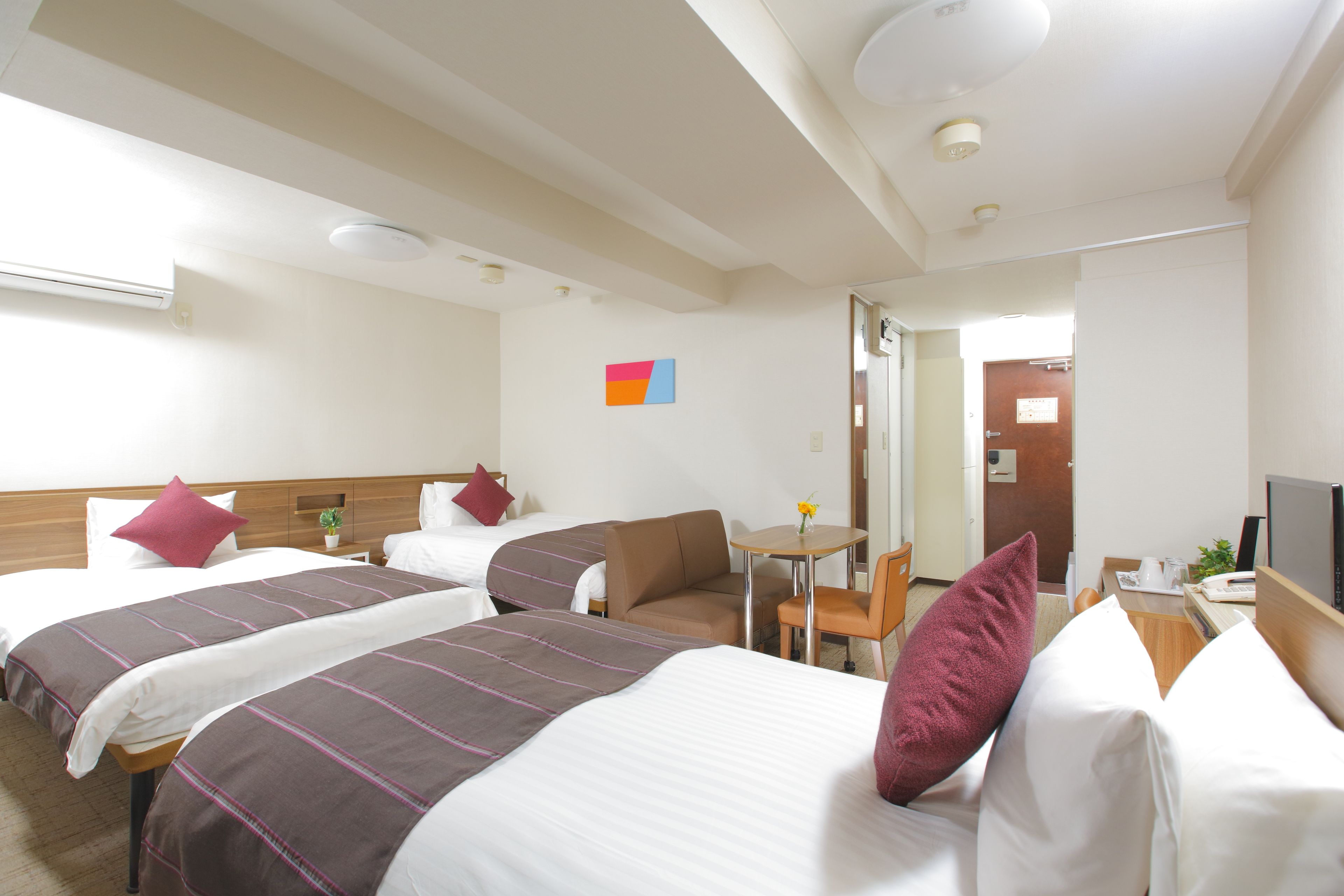 A hotel room with two beds, a desk, a chair, and a TV.