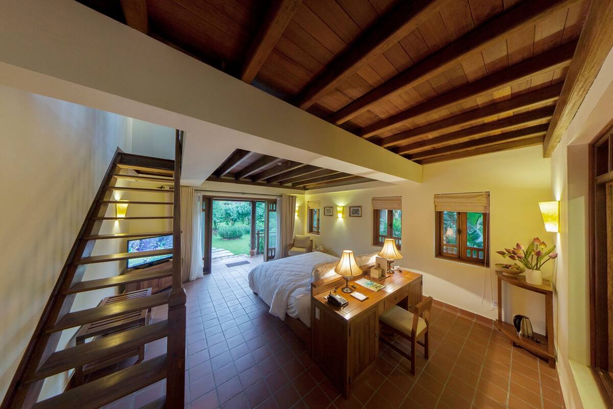 Quarto com cama, mesa de cabeceira, luminária e vista para o exterior.