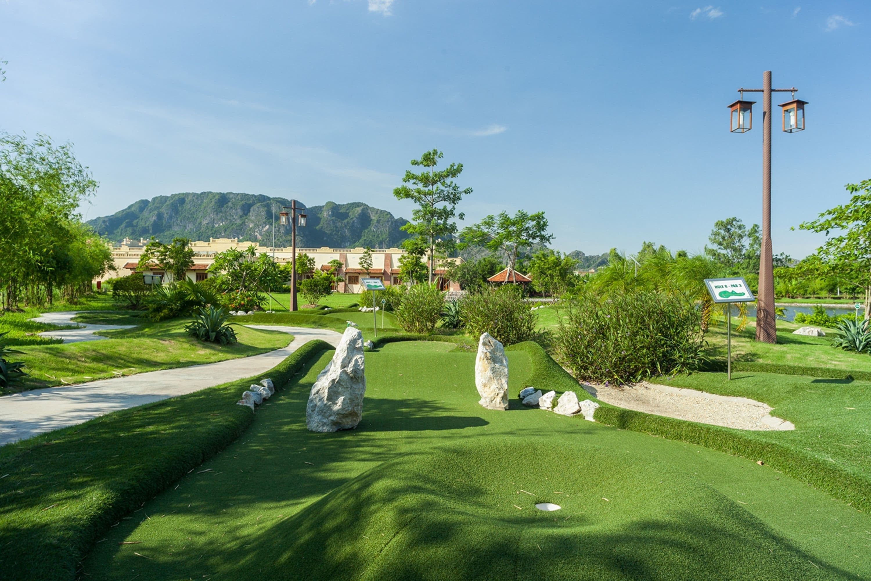 A well-maintained golf course with a clear path, large rocks, and a distant building complex.