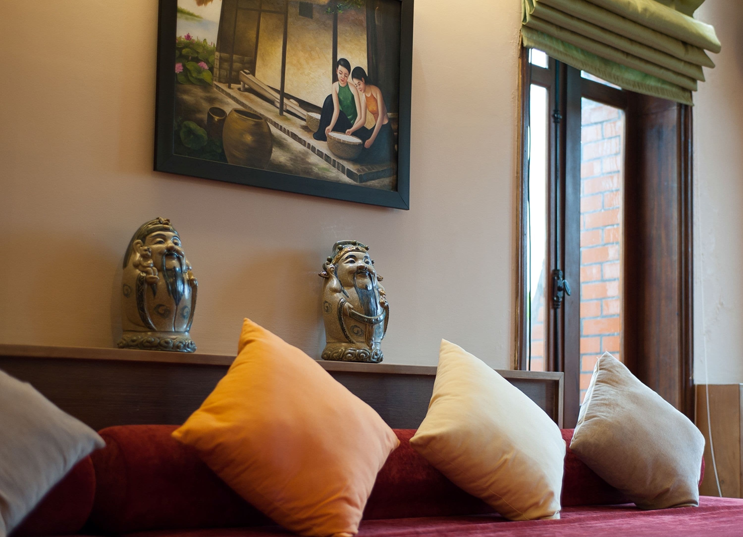 A room with a bed, pillows, a painting, and two decorative figures.