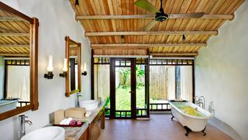 Un baño con techo de madera, una bañera independiente, un espejo grande y vistas a la vegetación exterior.