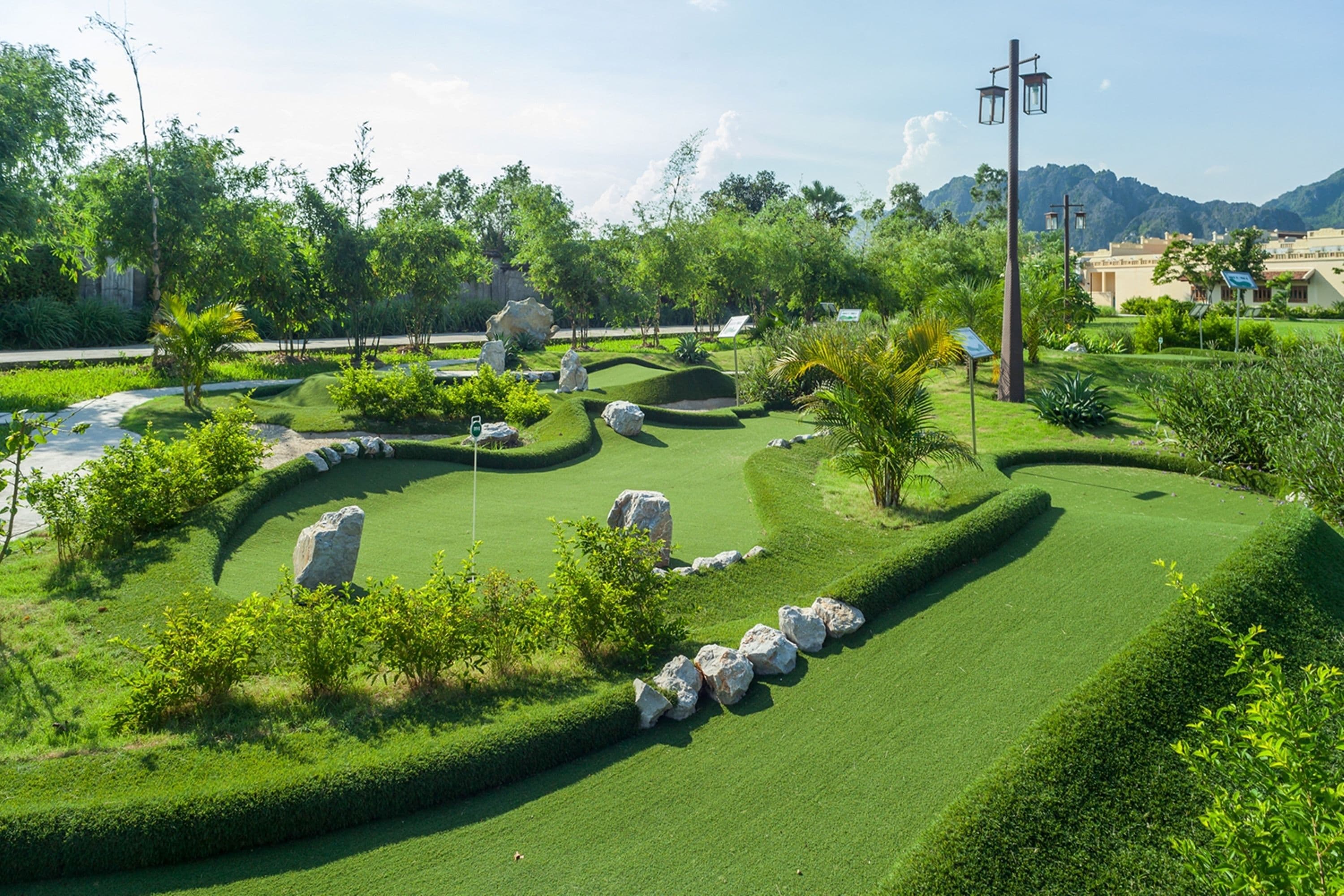 A well-maintained golf course with neatly trimmed grass, rock formations, and a variety of trees and shrubs.