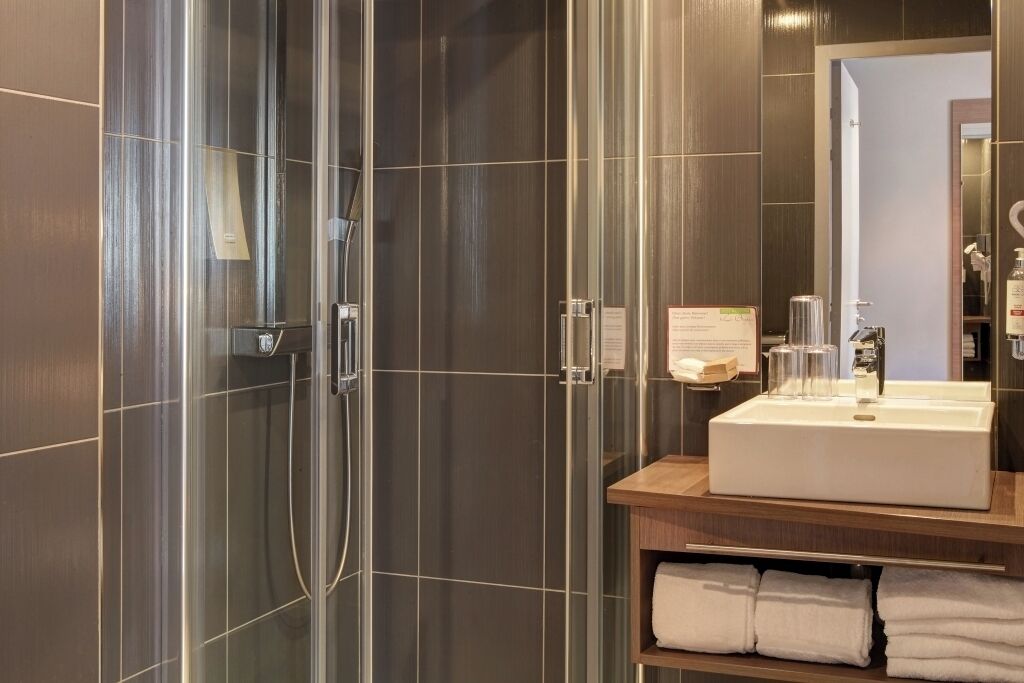 A modern bathroom with a glass shower enclosure, a wooden vanity with a white sink, and a mirror above it.