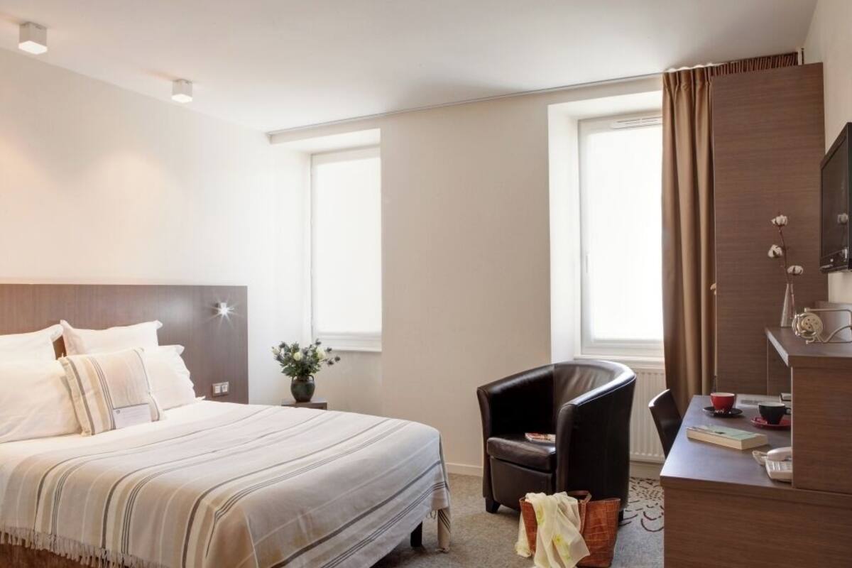 Une chambre d’hôtel avec un lit, un bureau, une chaise, une télévision et une fenêtre.