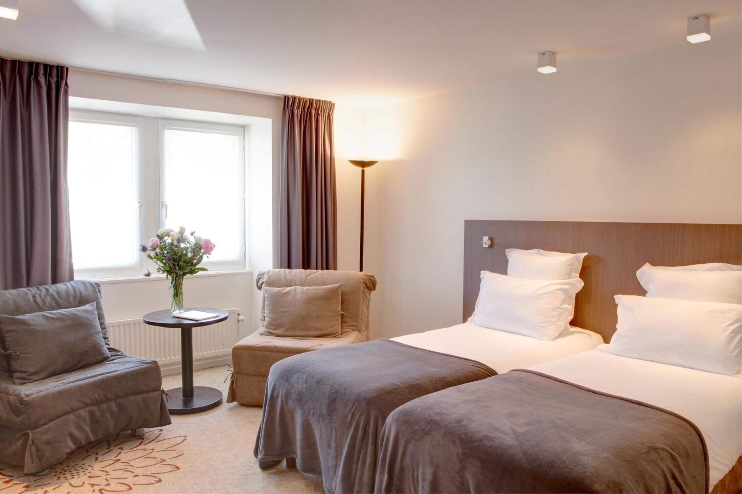 Hotellihuone, jossa on kaksi sänkyä, sohva, pieni pöytä maljakolla ja lamppu.