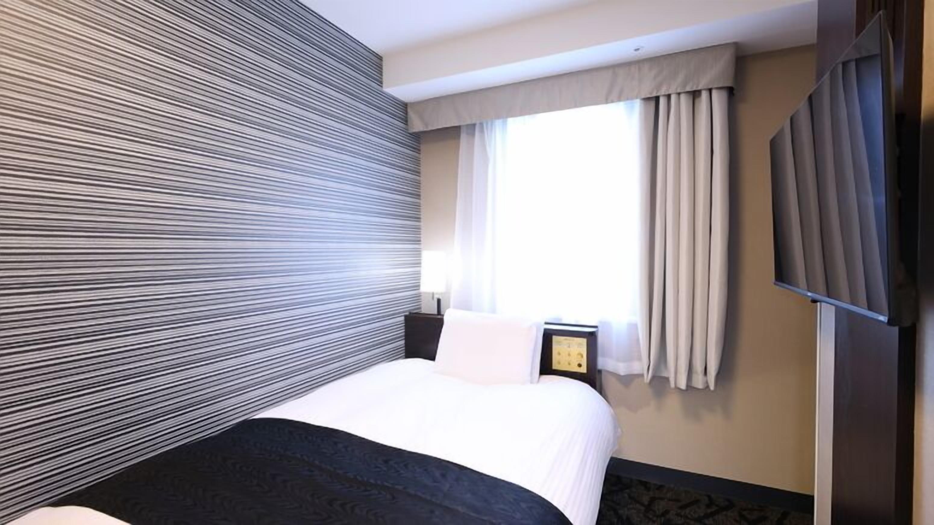 A hotel room with a bed, a bedside table, a TV, and a window with curtains.