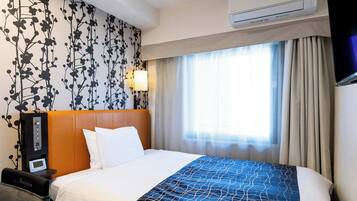 A hotel room with a bed, a bedside table with a lamp, an air conditioning unit, and a window with curtains.