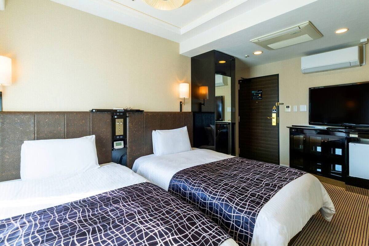 Ein Hotelzimmer mit zwei Betten, einem Fernseher, einem Schreibtisch und einem Spiegel.