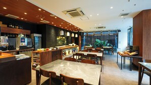 A modern restaurant interior with marble tables, wooden chairs, a bar area with a Pepsi machine, and large windows offering a view of greenery.