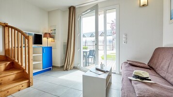 Um apartamento moderno com escada de madeira, um armário azul, um sofá cinza e uma porta de vidro deslizante para uma área externa.