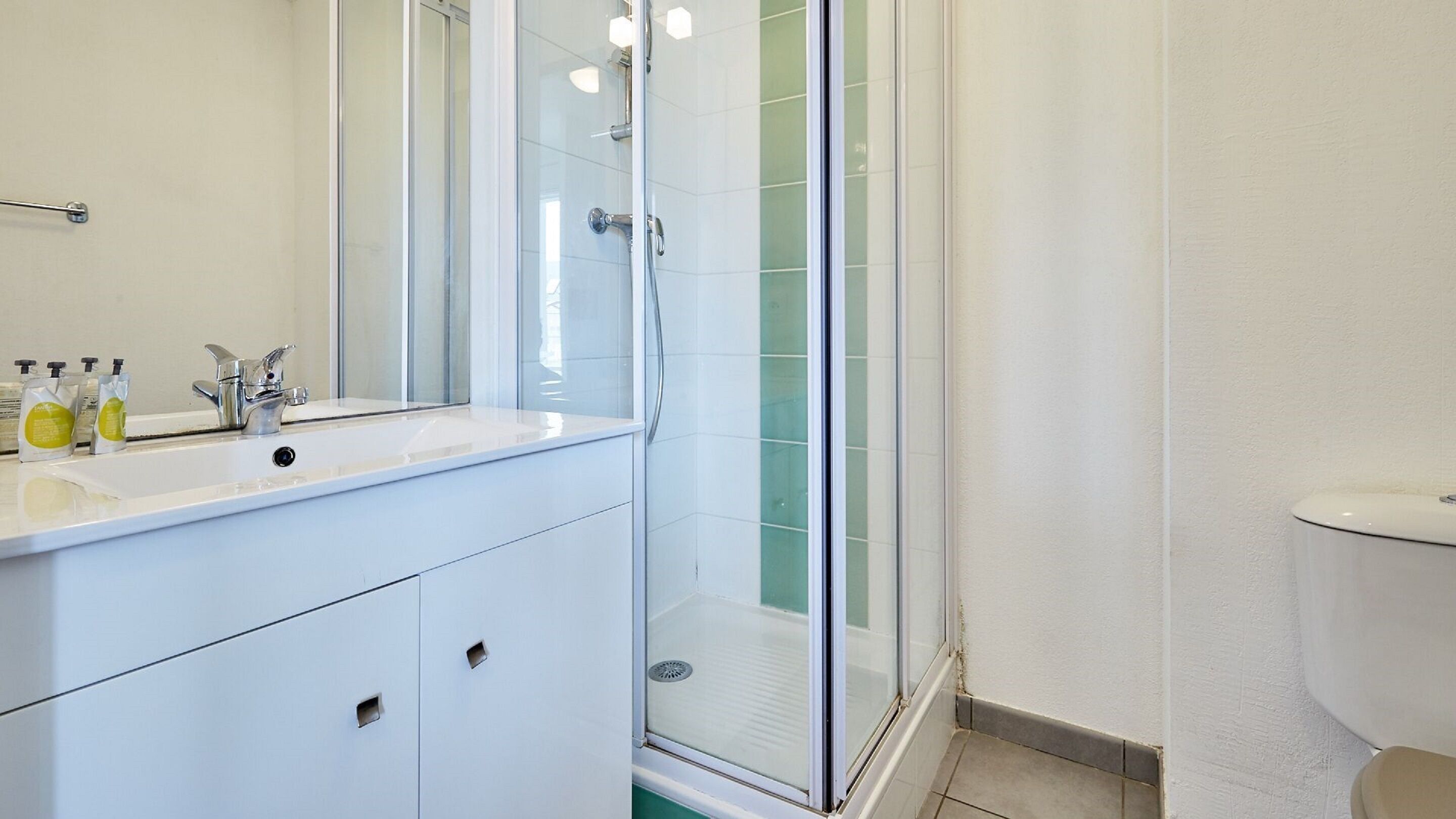 Un baño con lavamanos blanco, espejo y cabina de ducha.