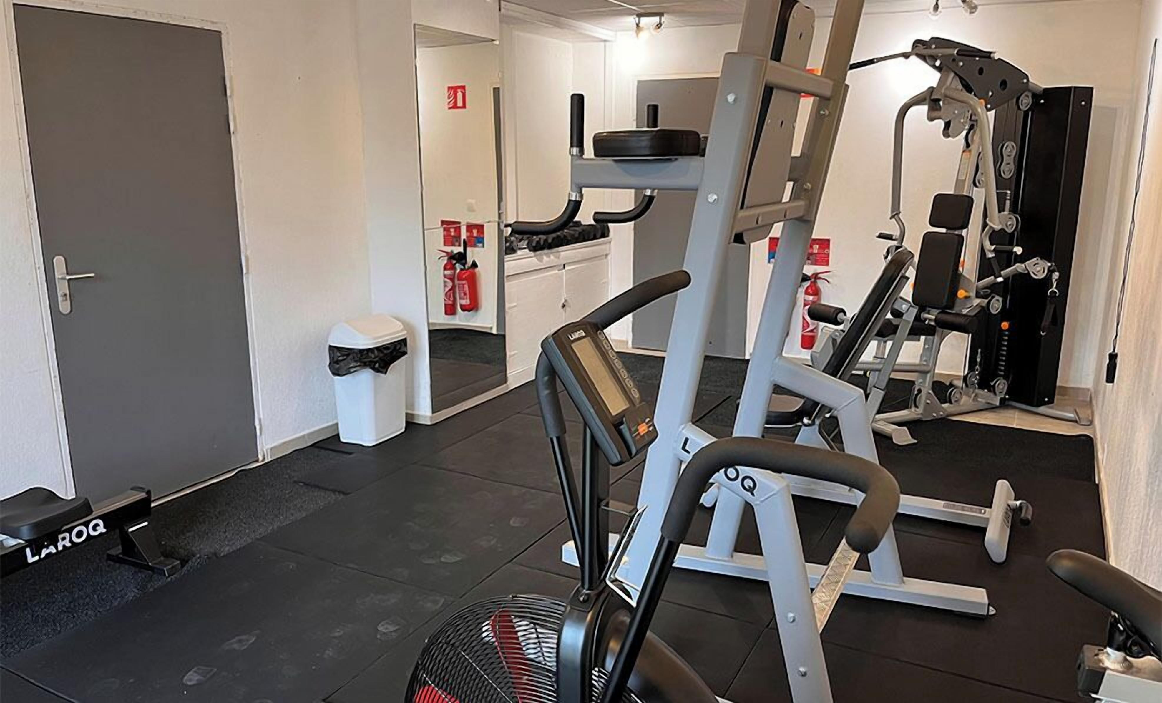 A gym with exercise equipment, a door, and a trash bin.