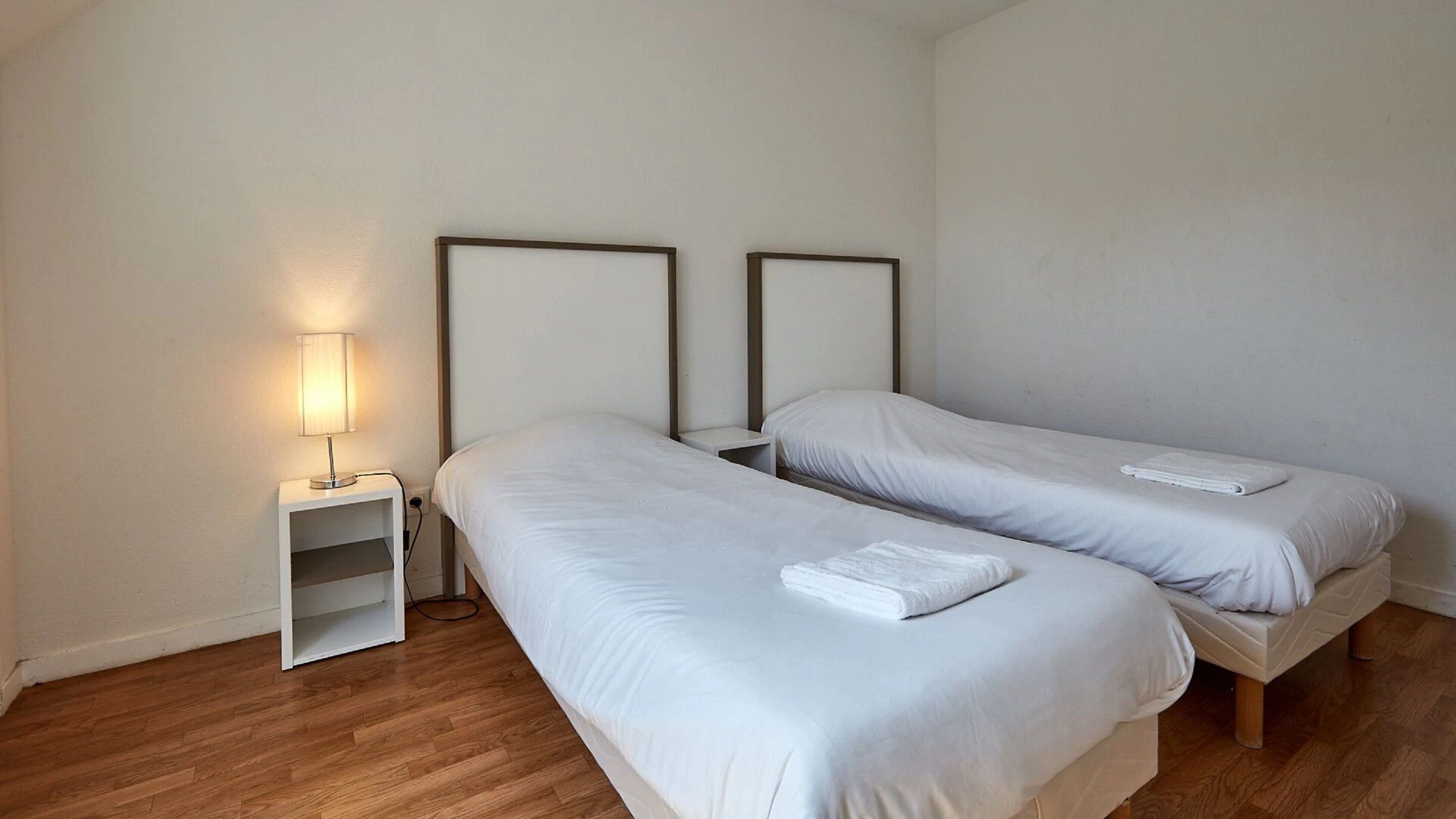 Ein Schlafzimmer mit zwei Einzelbetten, einem Nachttisch mit Lampe und einer kleinen Regalwand.
