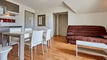 Een moderne woonkamer met een bruine bank, een eettafel met stoelen, een keuken met kasten en een koelkast, en een deur naar een andere kamer.