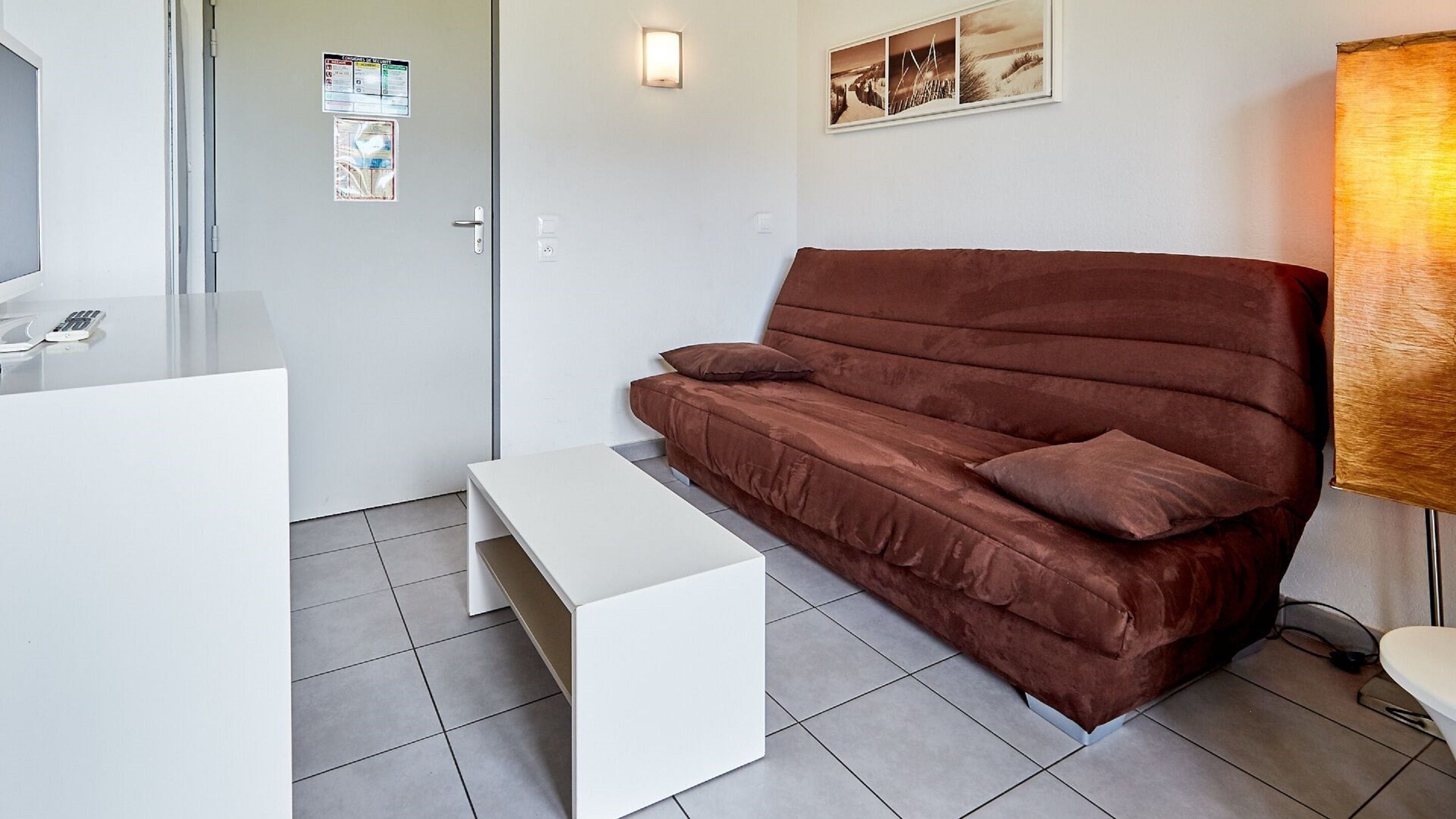 A modern, minimalistic room with a brown sofa, a white coffee table, and a small white desk with a computer and a phone.