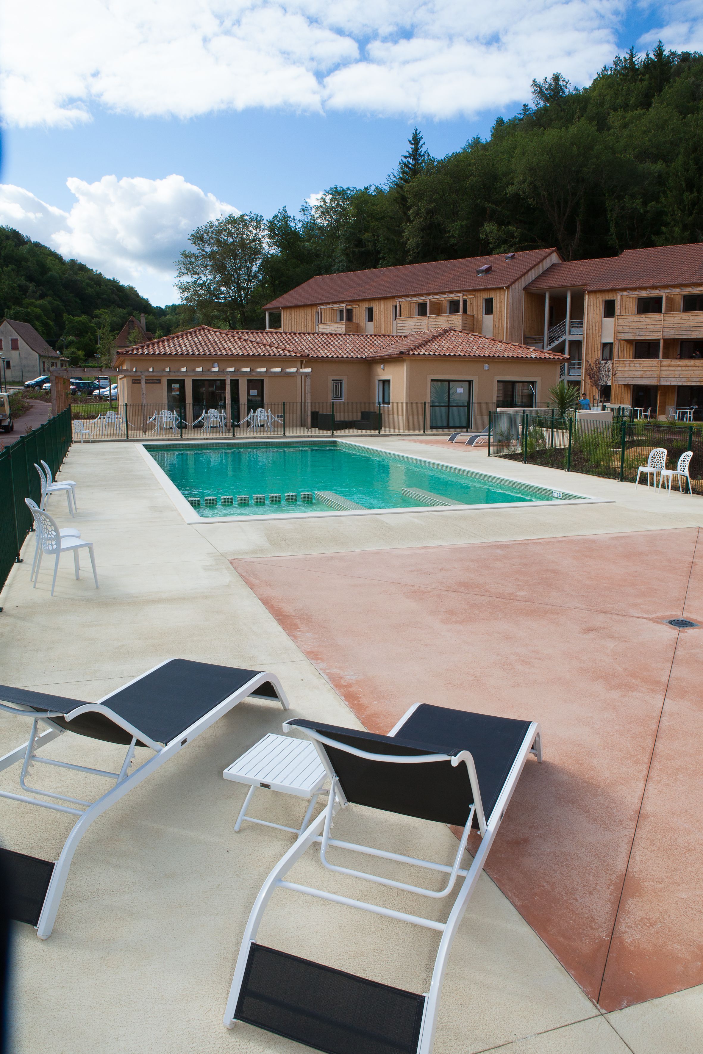 Un área de piscina con sillones de descanso y un edificio con tejado de azulejos.