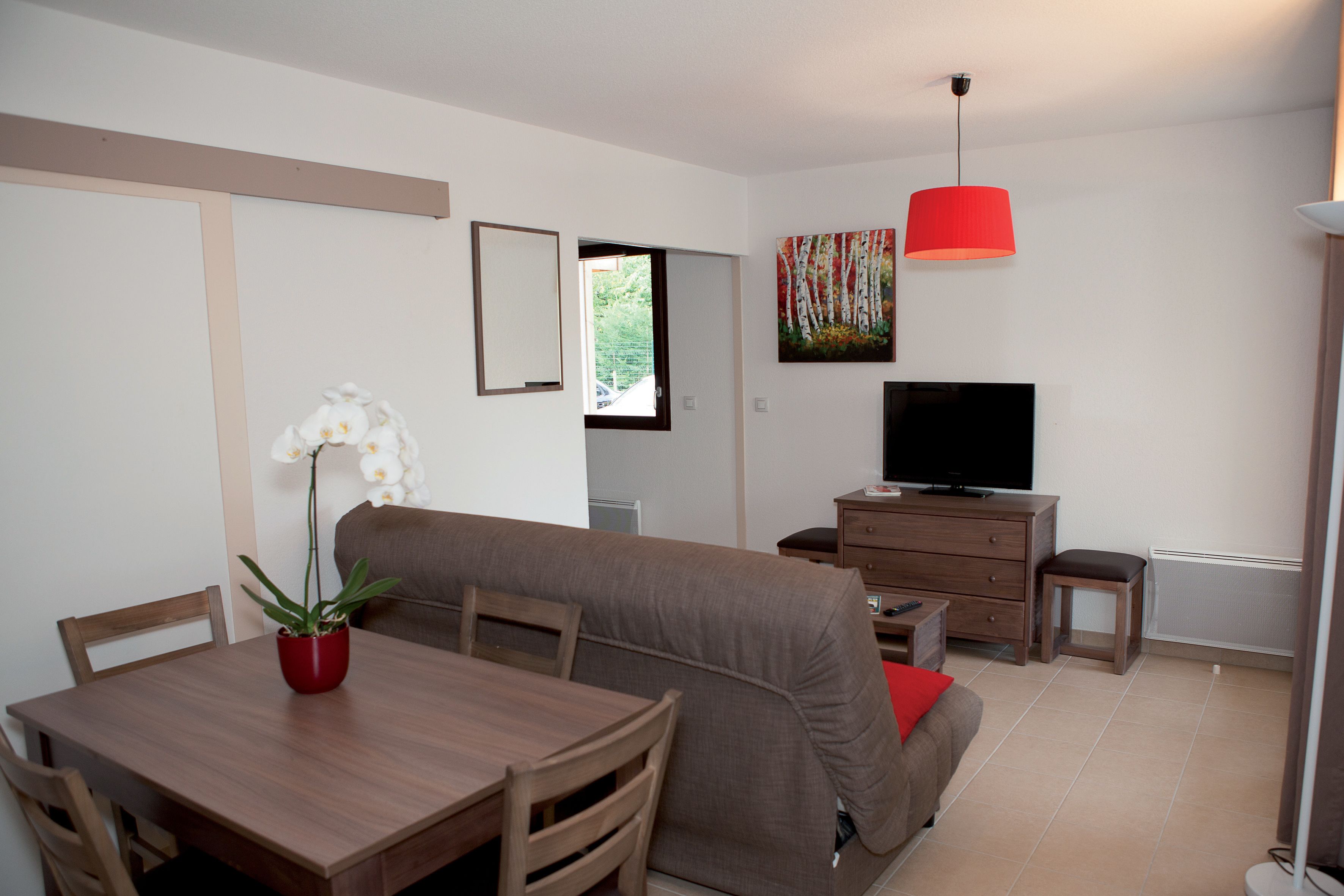 En kompakt opholdsstue med spisebord, sofa, fjernsyn og en potteplante.
