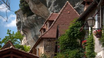 A traditional stone building with a steep roof, surrounded by lush greenery and a prominent rock formation in the background.
