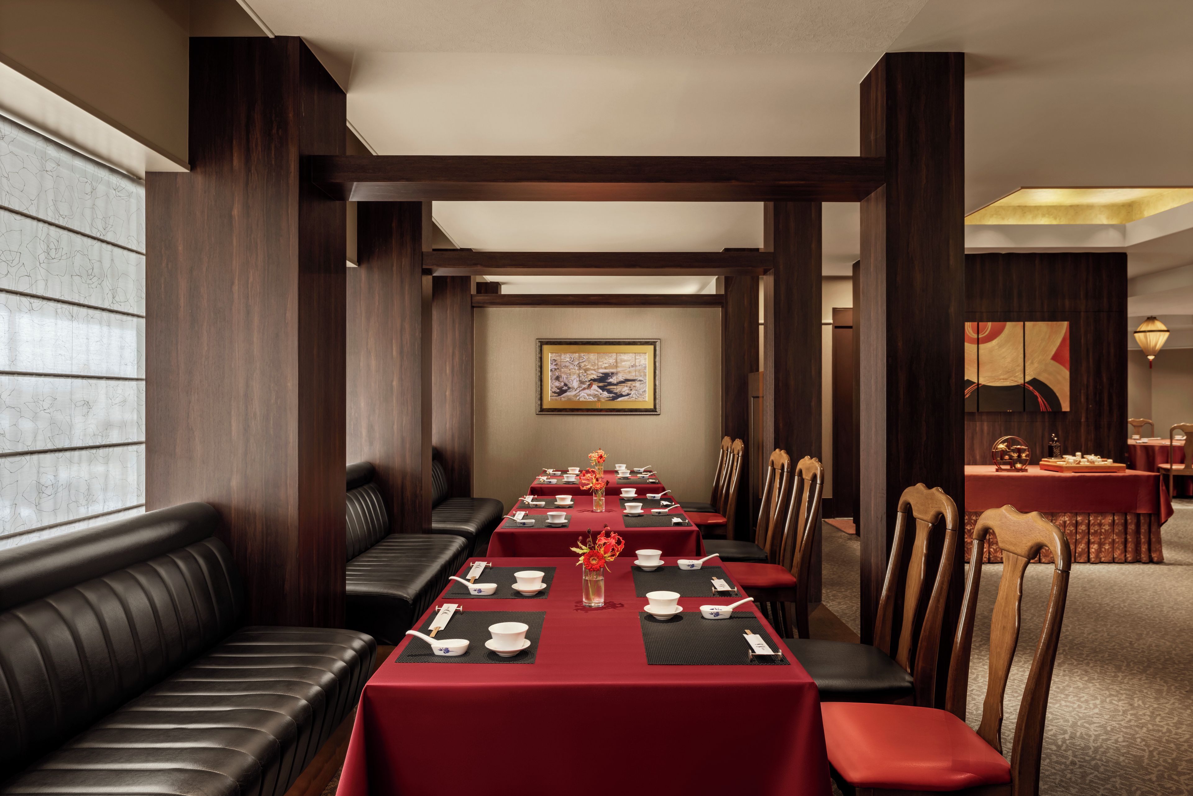Un restaurante con una larga mesa de comedor, manteles rojos y asientos de cuero negro.
