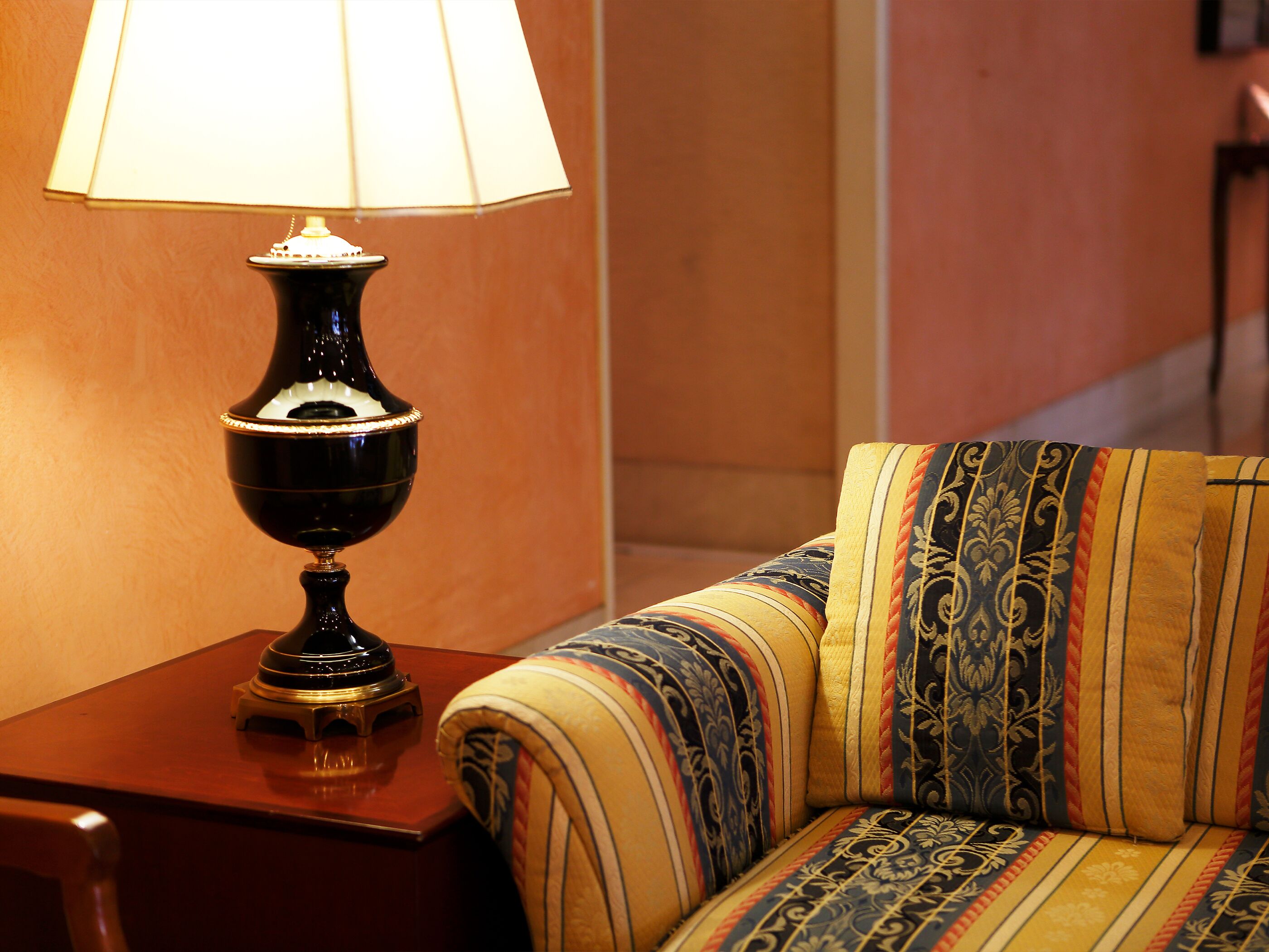 A lamp on a wooden side table next to a sofa with a patterned cushion.
