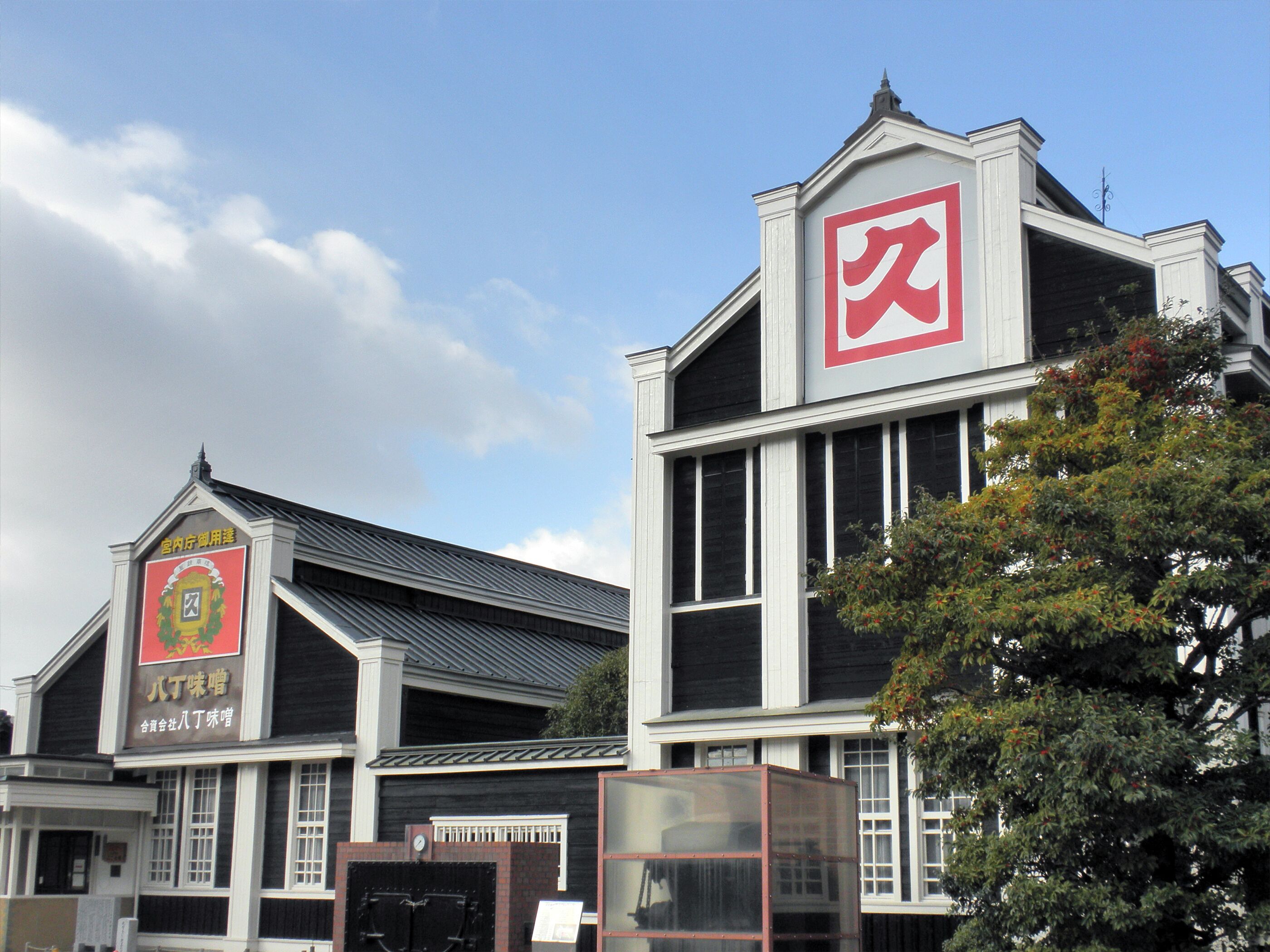 A building with a large red square sign on the top right, a smaller sign with Chinese characters on the left, and a black gate in the center.