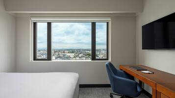 Une chambre d’hôtel équipée d’un lit, d’un bureau, d’une chaise et d’une grande fenêtre donnant sur la ville.