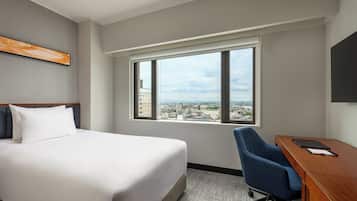 A hotel room with a bed, a desk, and a window with a city view.
