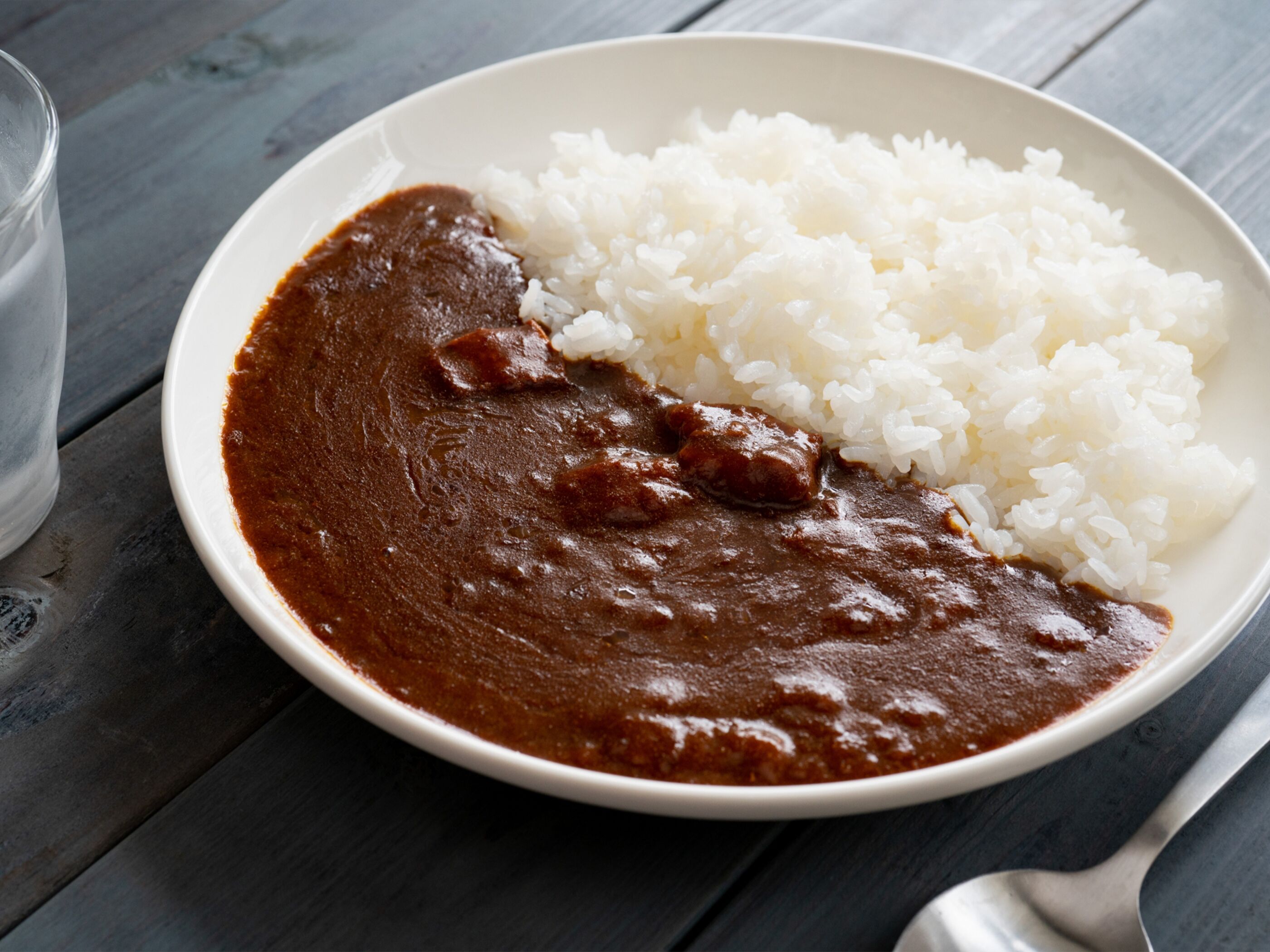 A white bowl with a dark brown sauce and white rice on a wooden table.