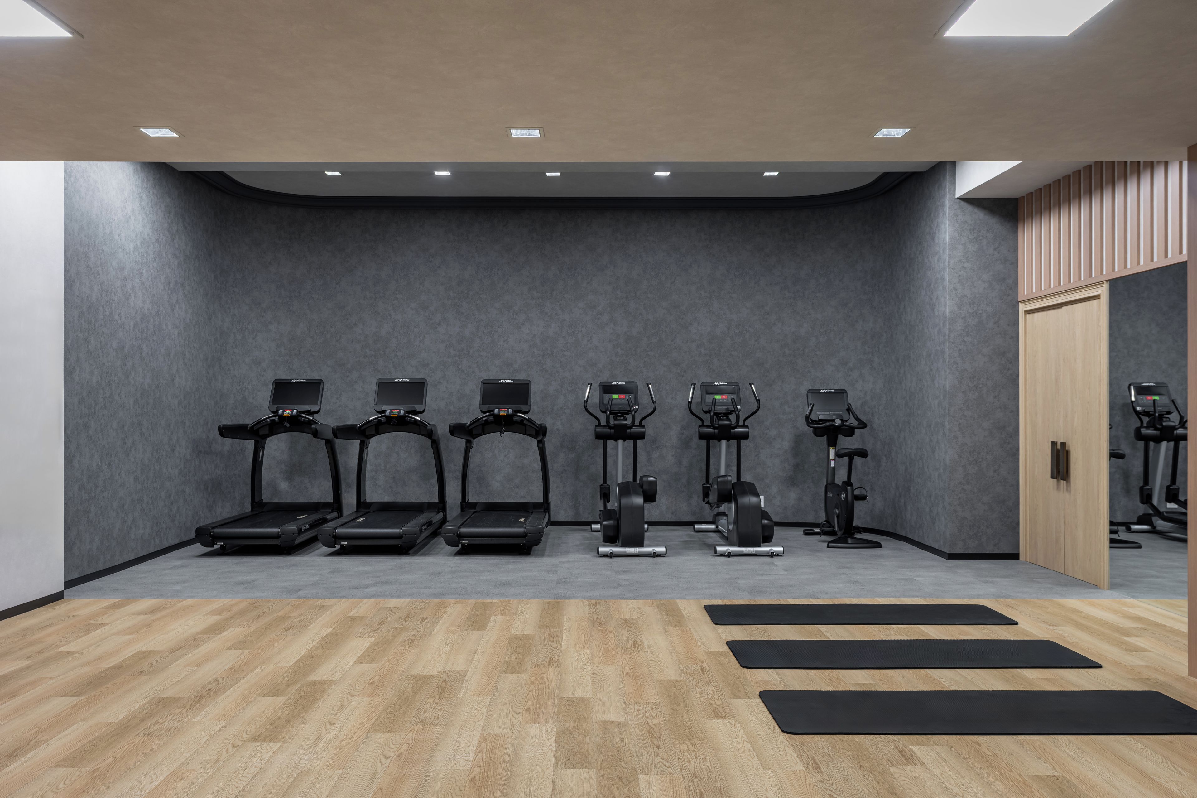 A gym with treadmills, elliptical machines, and a wooden floor.