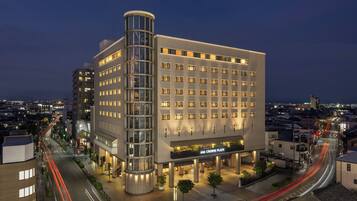 Un hotel de varios pisos con un diseño moderno, que presenta una llamativa estructura de vidrio curva a la izquierda y una fachada plana a la derecha.