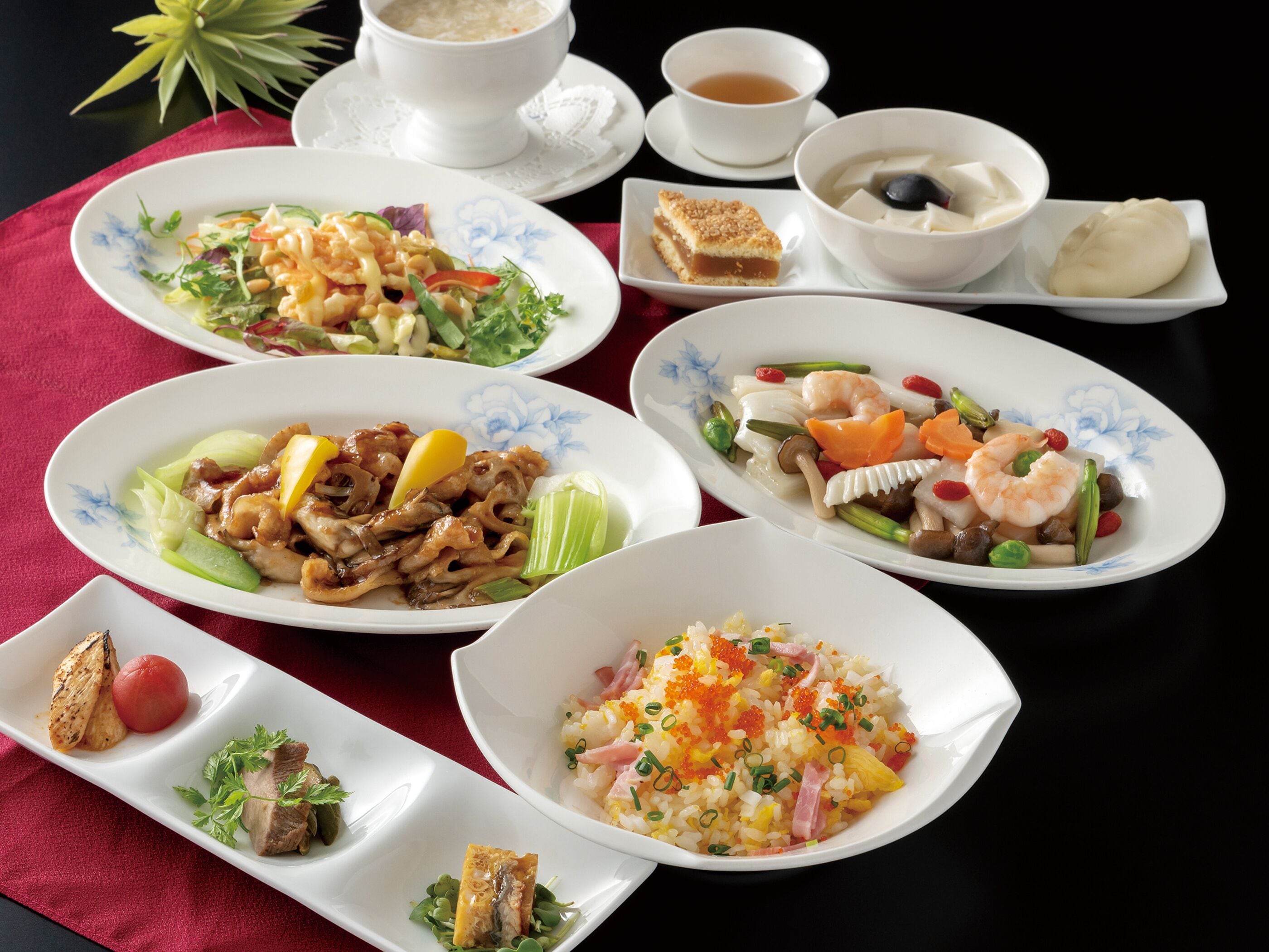 Une variété de plats sont disposés sur la table, notamment une salade, des nouilles et du riz agrémenté de différentes garnitures.