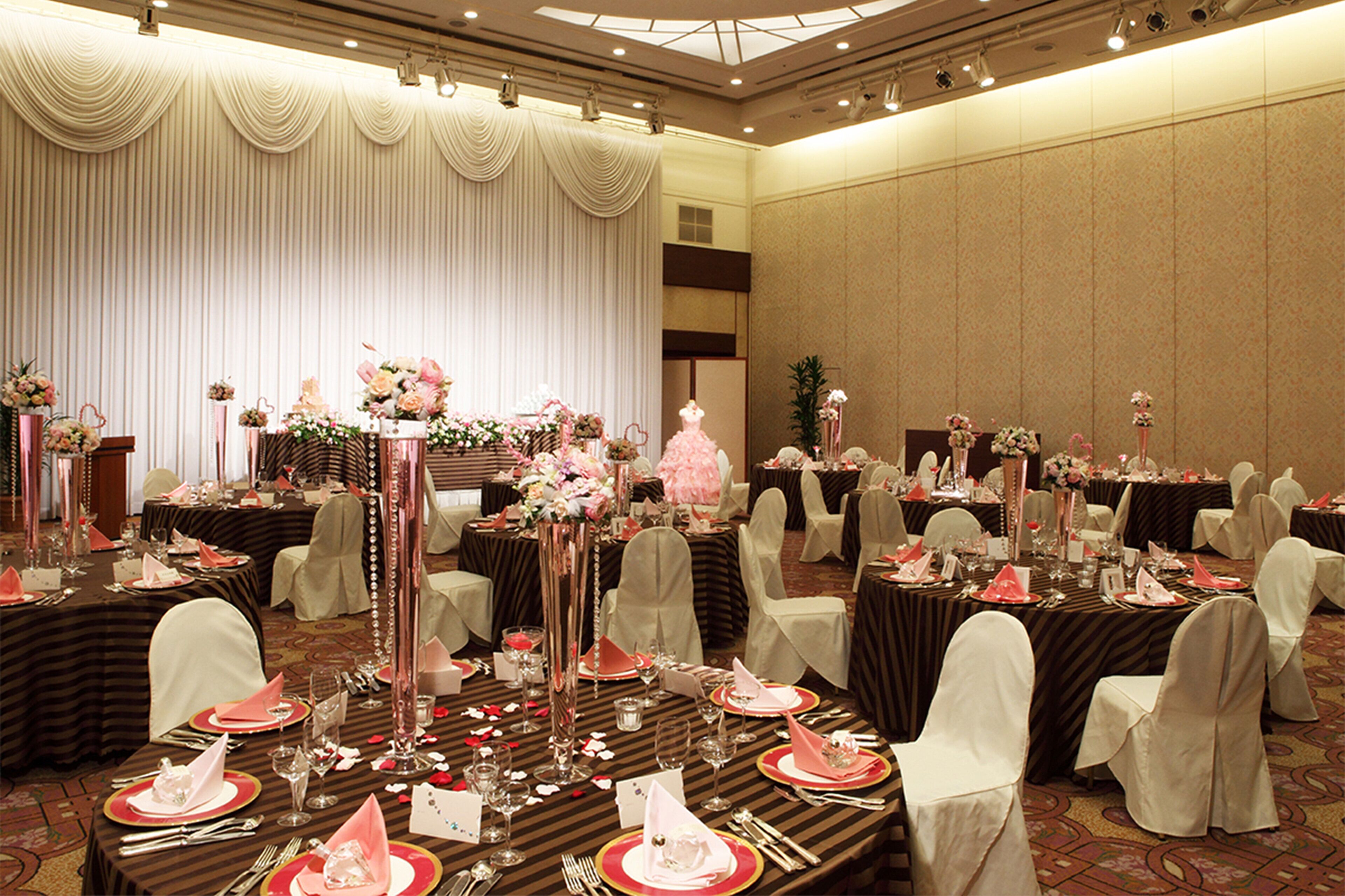 A banquet hall with round tables set for a formal event, featuring floral centerpieces and white chairs.
