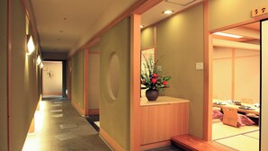 Un pasillo de hotel con una recepción, un banco de madera y una planta pequeña.