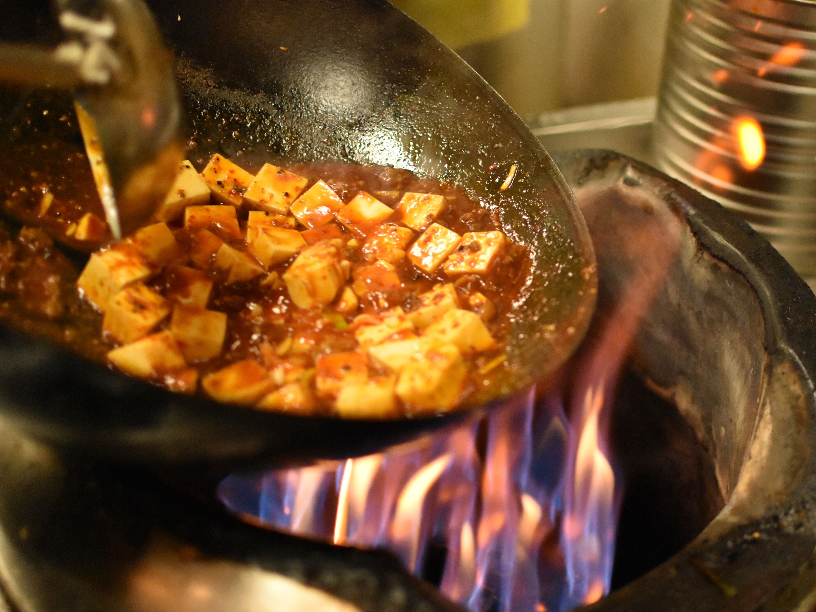 Ein Wok mit Tofu und Sauce wird über offener Flamme gebraten.