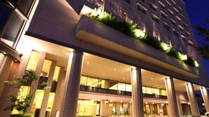 Un hotel moderno con una entrada amplia, varios pisos y un paseo cubierto con vegetación.