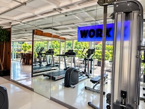 Une salle de sport équipée de matériel d’exercice, avec un panneau indiquant « TRAVAIL » et une vue sur la verdure à l’extérieur.