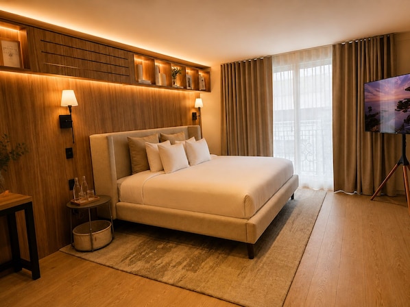 Habitación de hotel con una cama grande, un televisor en un mueble bajo, cabecero de madera y vistas al exterior por la ventana.