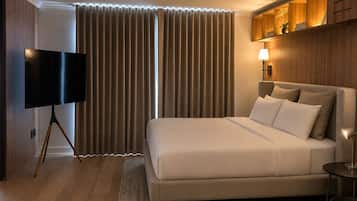 Habitación de hotel moderna con una cama grande, un televisor de pantalla plana y una mesita de noche con lámpara.