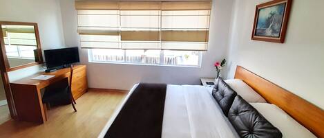 A hotel room with a bed, a desk, a television, and a window with blinds.
