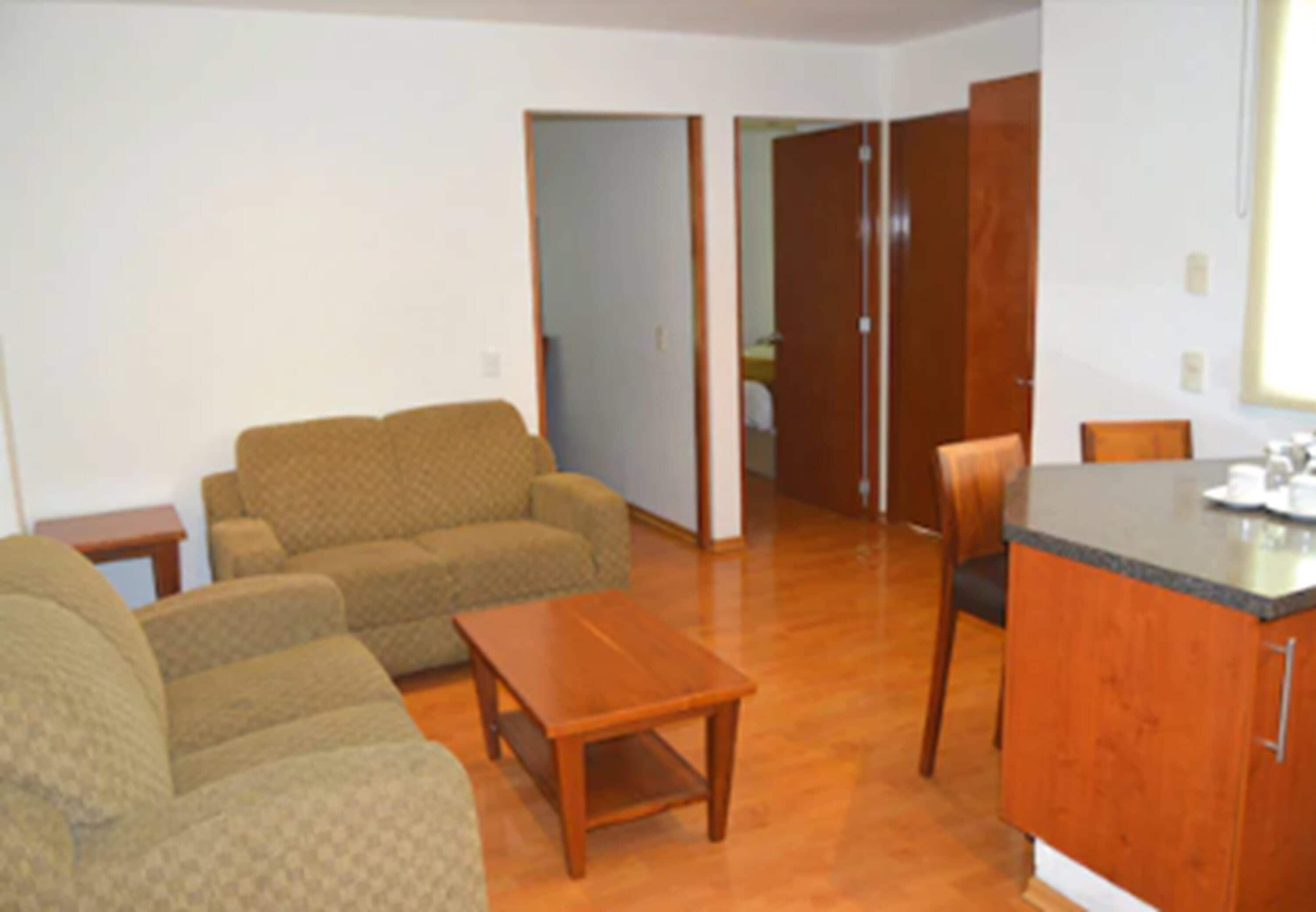 Una sala de estar con un sofá, una mesa de centro de madera y una zona de cocina con encimera y armarios.