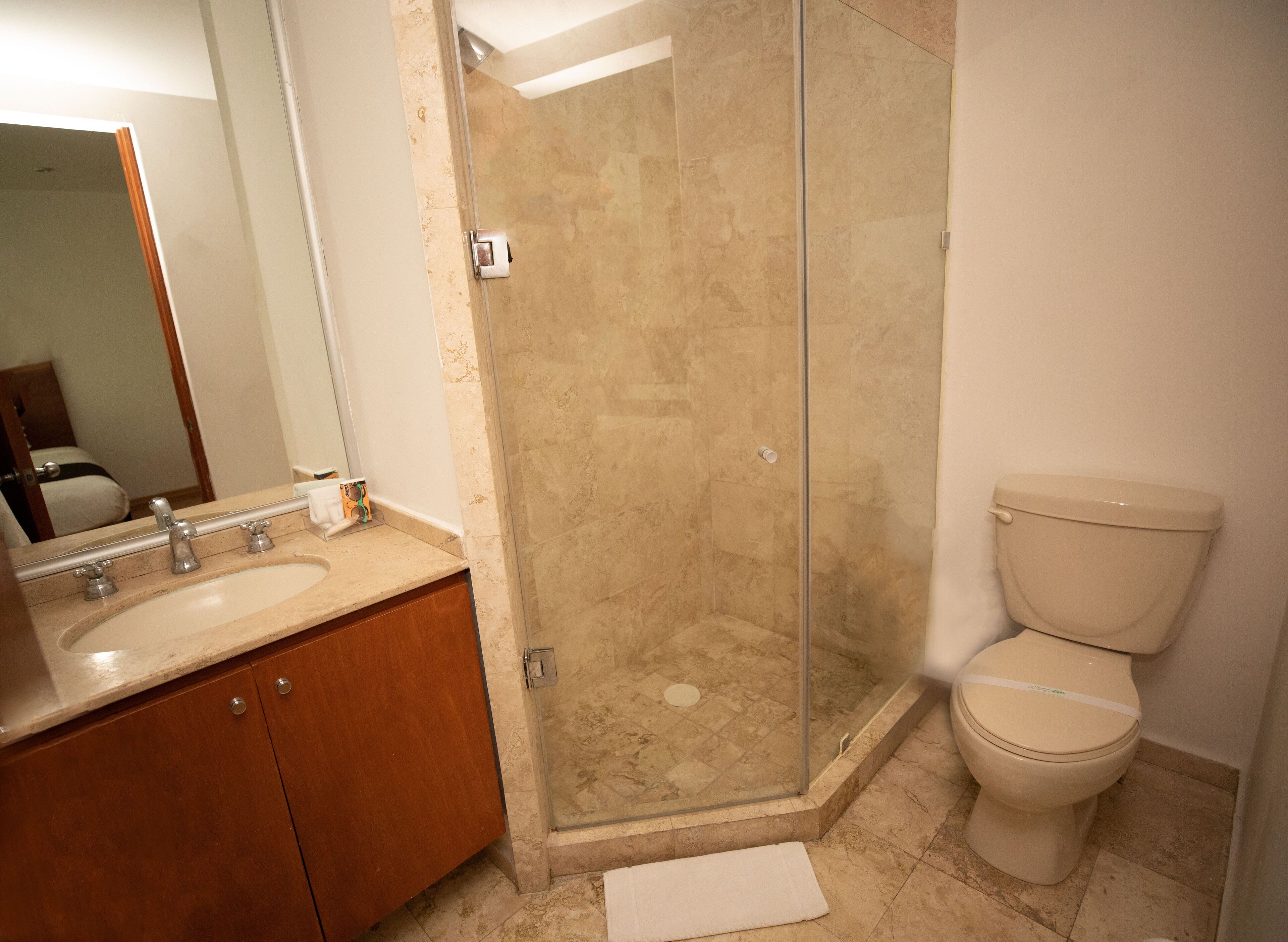 Un baño con ducha de vidrio, inodoro y lavamanos con gabinete de madera.