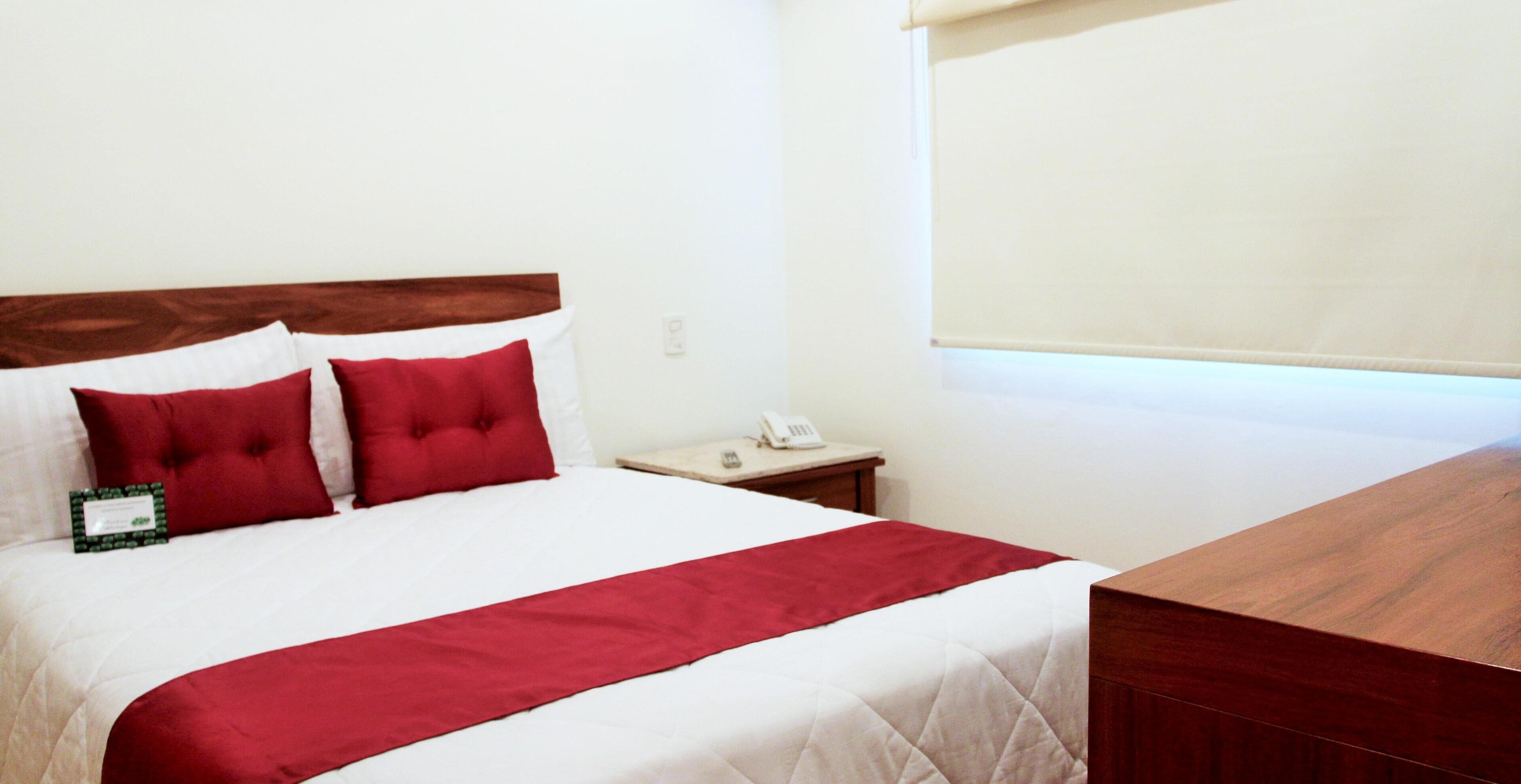 Une chambre d’hôtel avec un lit, une tête de lit en bois, une table de chevet avec un téléphone et une fenêtre avec un store.