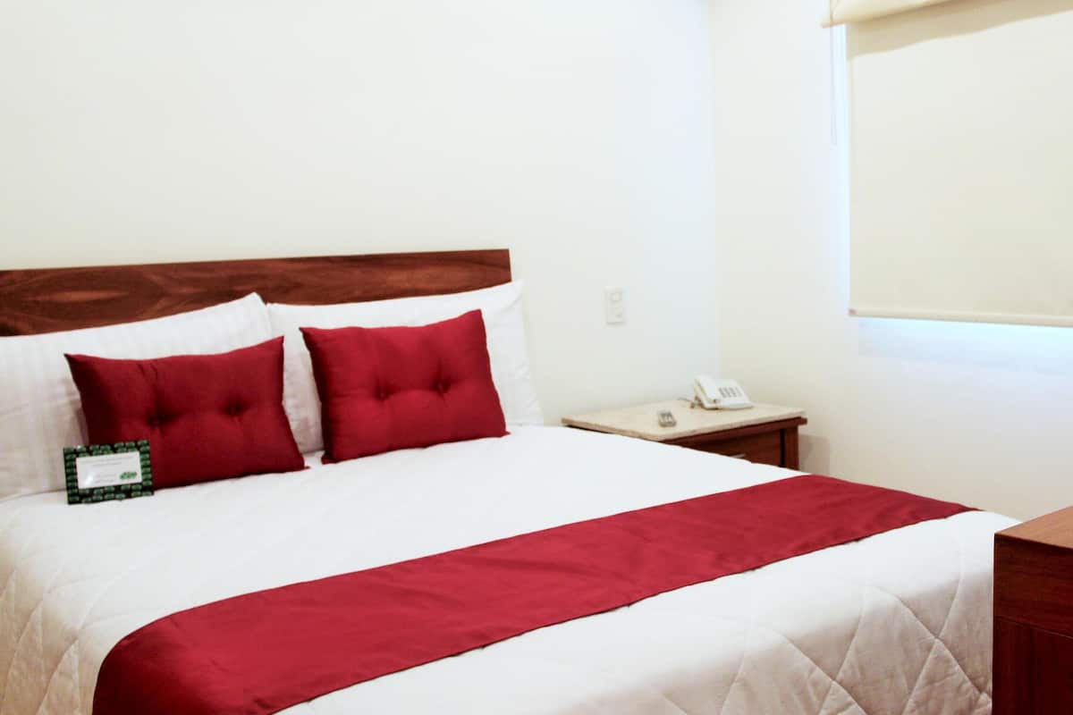 Une chambre d’hôtel avec un lit, une tête de lit en bois, une table de chevet avec un téléphone et une fenêtre avec un store.