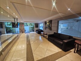 A lobby with a tiled floor, a black leather sofa, a coffee table, and a painting on the wall.