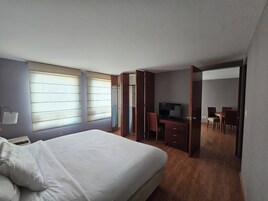 A hotel room with a large bed, a desk with a chair, a television, and a wardrobe.