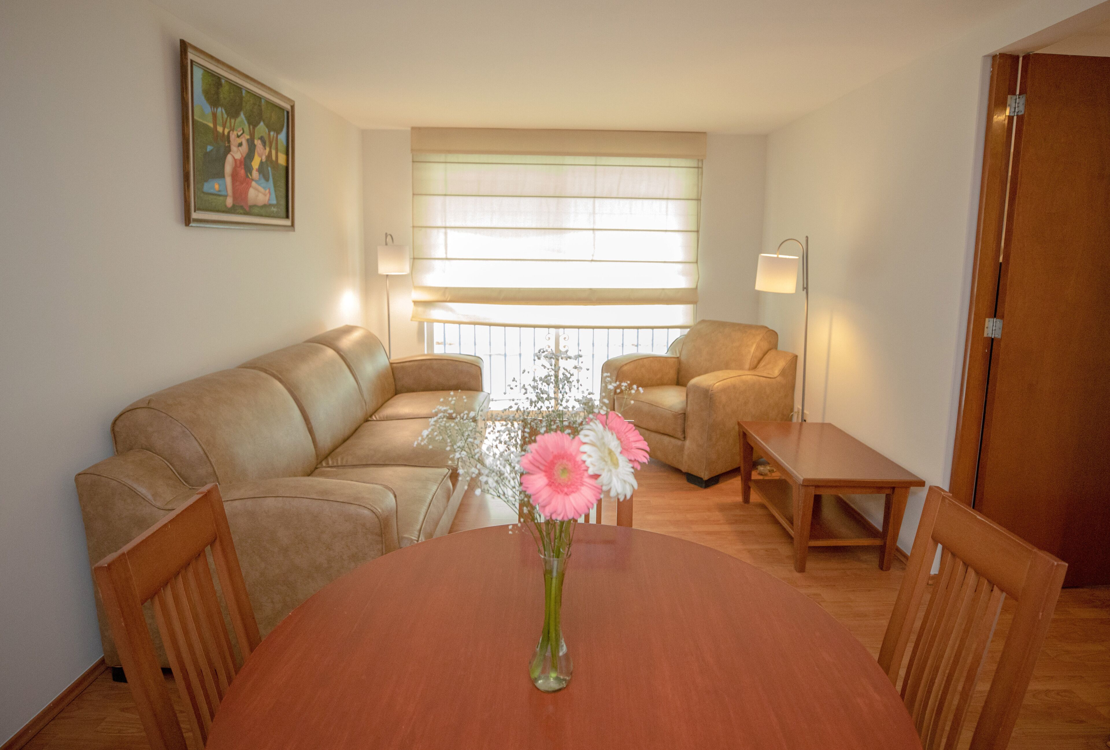 Una sala de estar con una mesa de comedor de madera, dos sofás y un jarrón con flores.